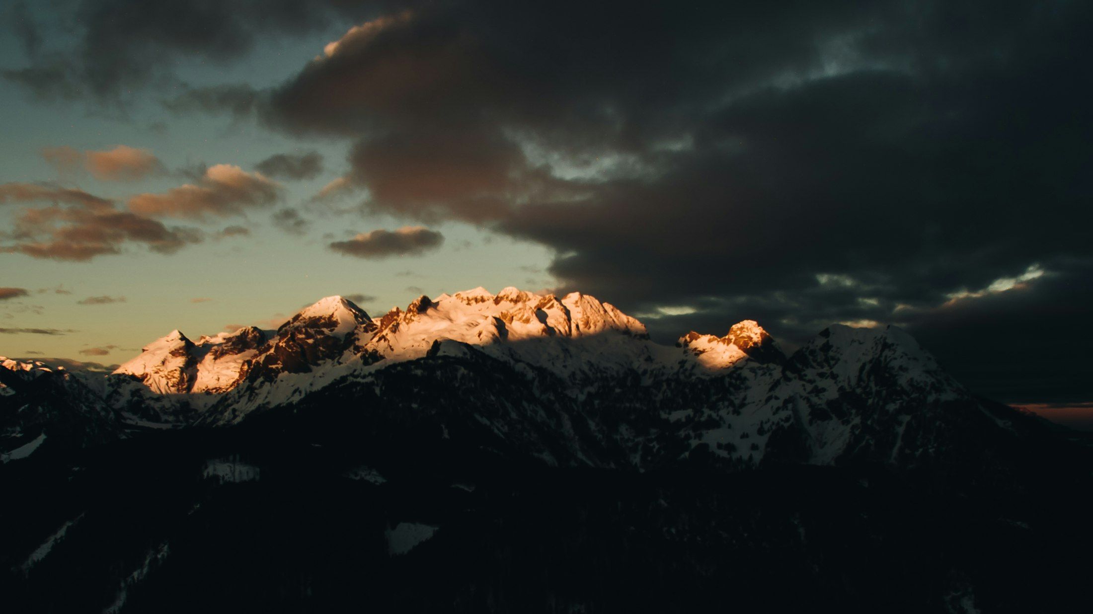 Schneebedeckte Gipfel im letzten Abendlicht unter dunklen Wolken